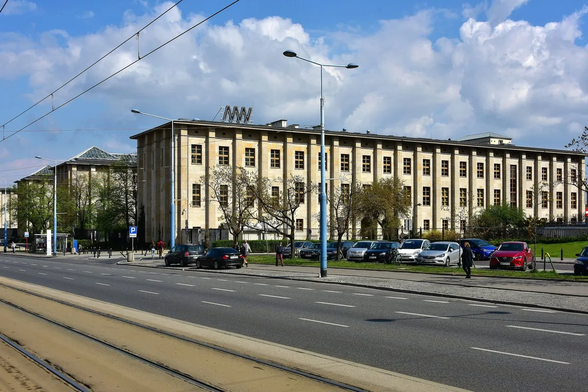 The long, pale stone main building of the National Museum in Warsaw seen across a wide street with tram tracks and trees