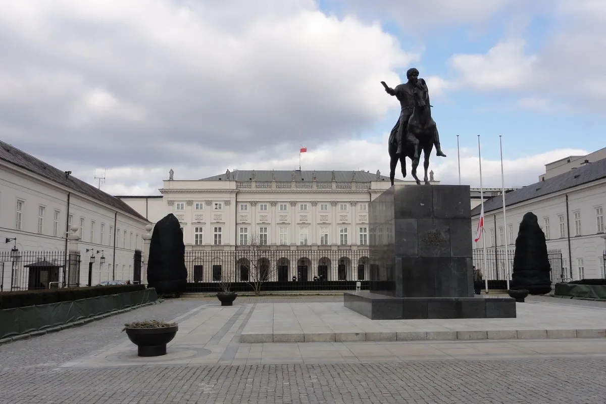 A pale classical palace behind a cobbled forecourt, with a bronze statue of a rider on a horse at the right